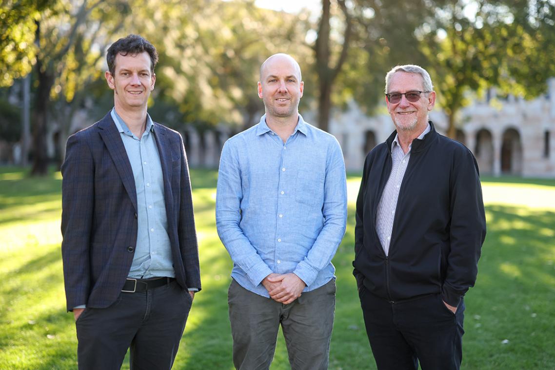 Three men standing in a grass field smiling at the camera 